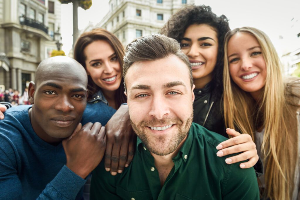 Un grupo de cinco personas sonrientes posando juntas al aire libre, transmitiendo amistad y diversidad en un entorno urbano.