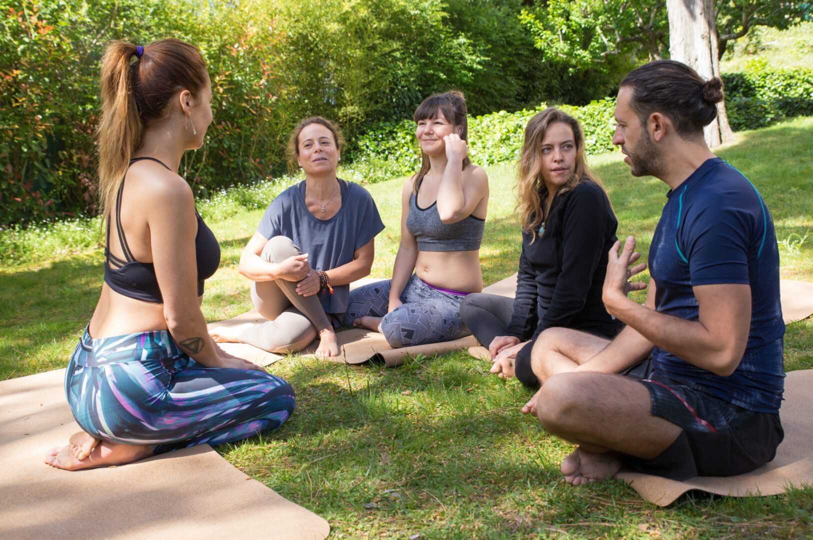 Grupo de personas haciendo yoga y meditando en un parque al aire libre.